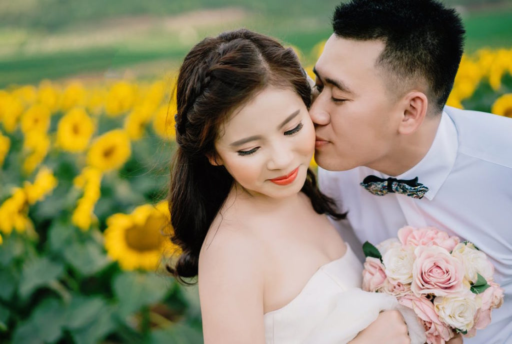 asian_couple_cheek_kisses_sunflower_field
