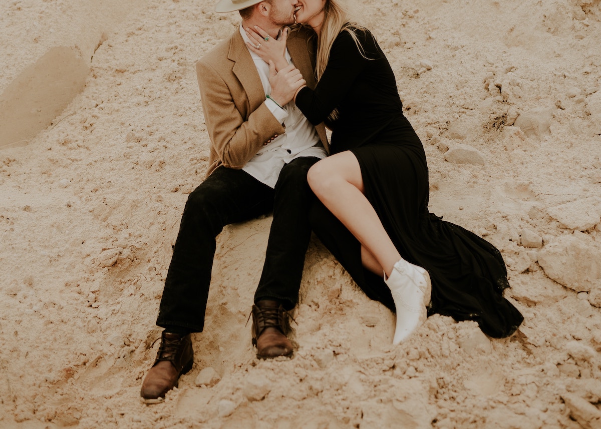 newly_engaged_couple_sitting_in_sand_kissing_embracing