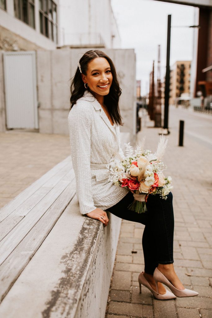 bride in sequin beaded blazer holding bouquet sitting on a bench