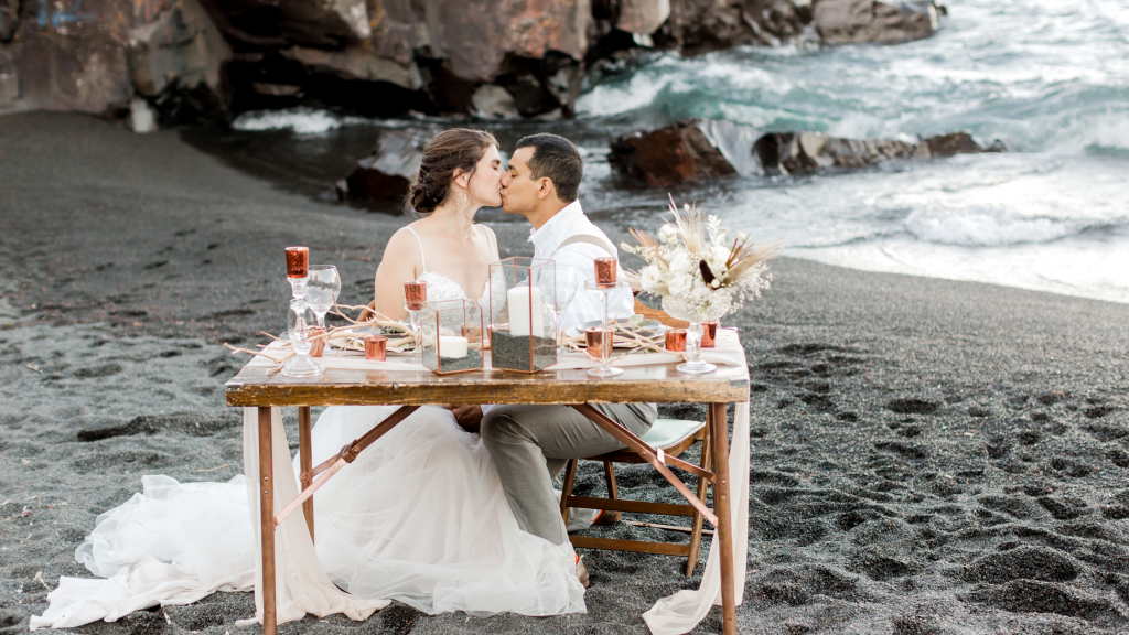bride and groom kissing at sweetheart table on beach