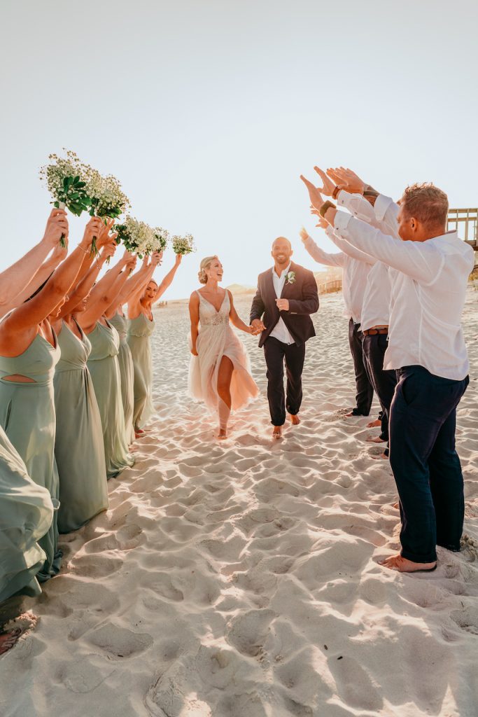 bride and groom running through friends arms on the beach
