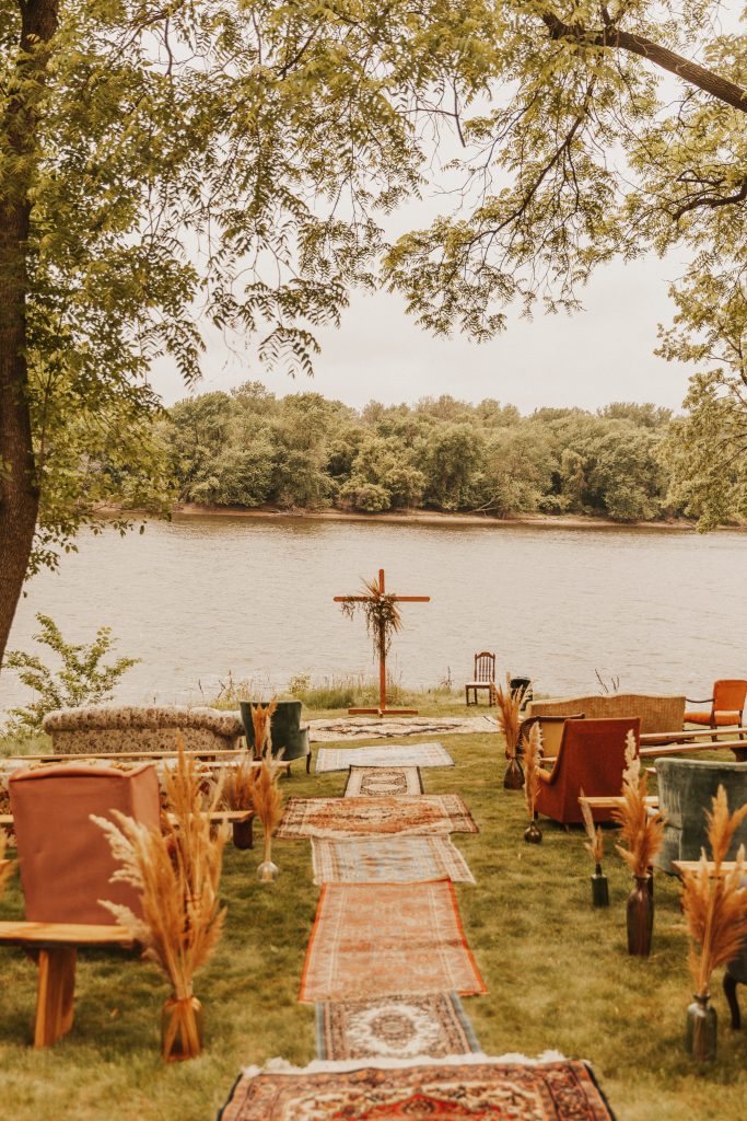 Outdoor wedding ceremony decorated with rugs, couches, and arm chairs