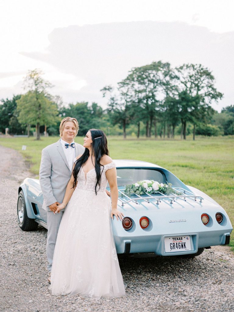 bride and groom standing in front of blue car
