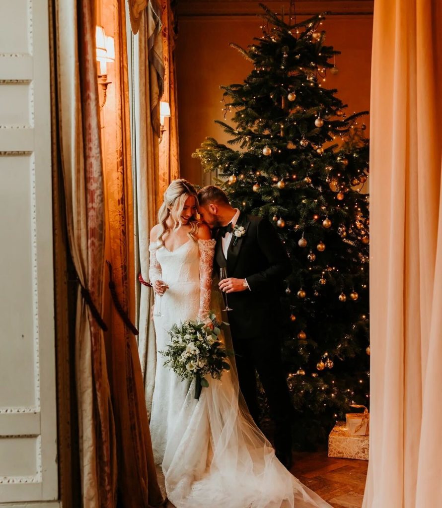 A couple embracing at their winter wedding complete with a Christmas tree