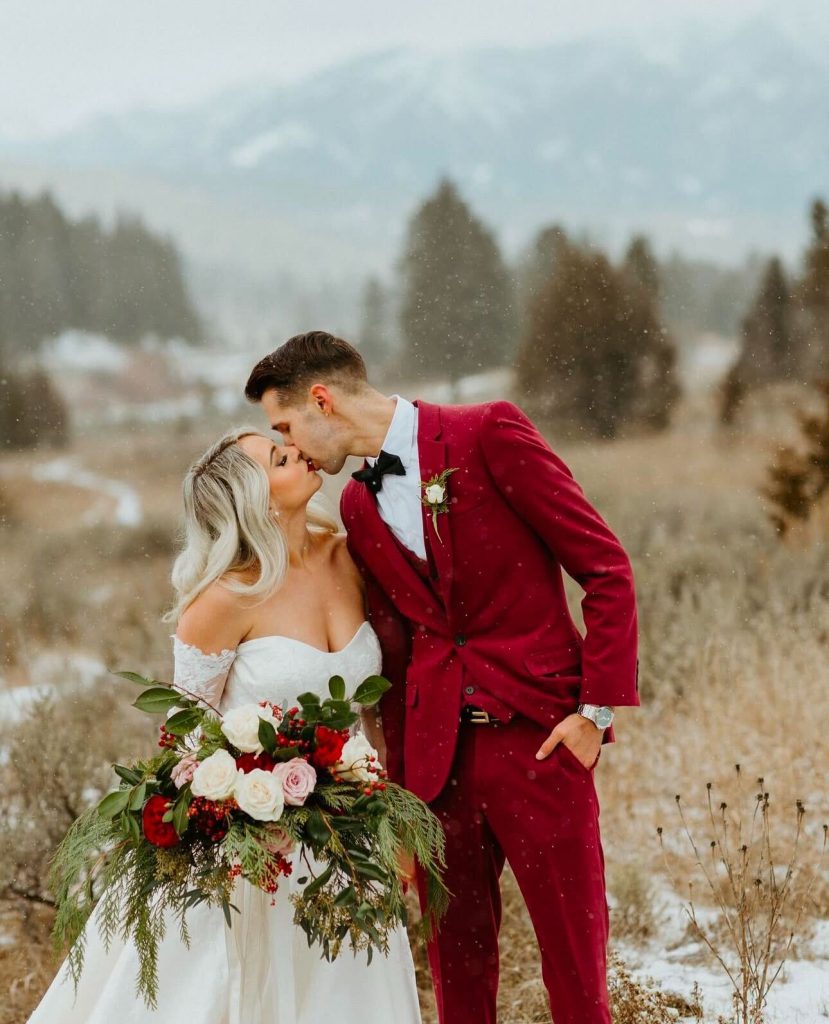 A couple kisses outdoors in a red suit at their winter wedding