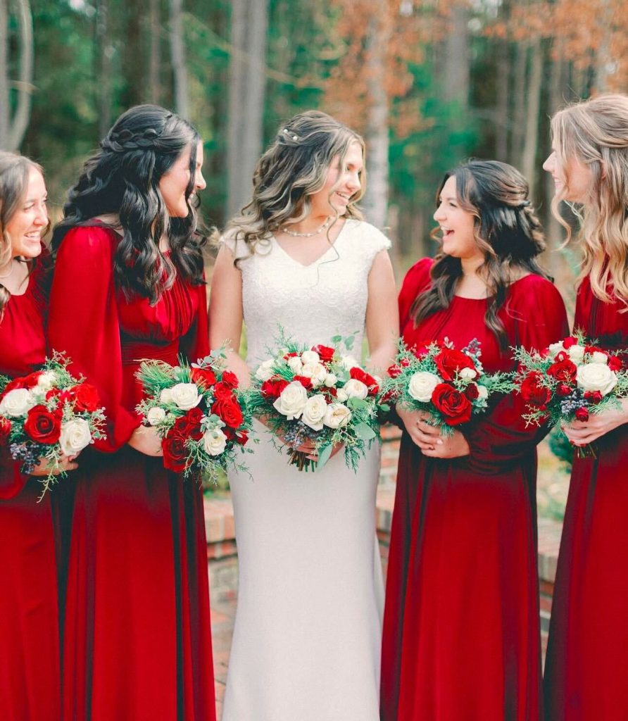 Bridesmaids in long sleeve red dresses standing next to a bride