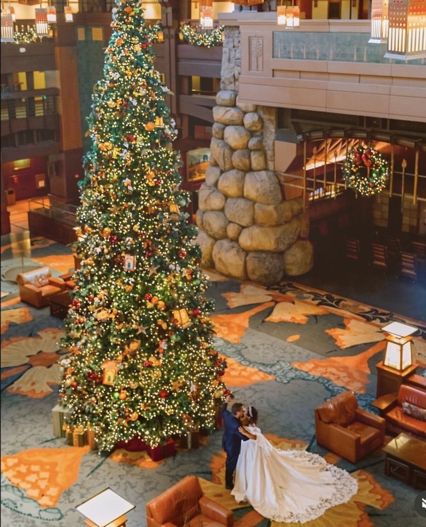 Newly married couple kissing next to a large Christmas tree at their winter wedding