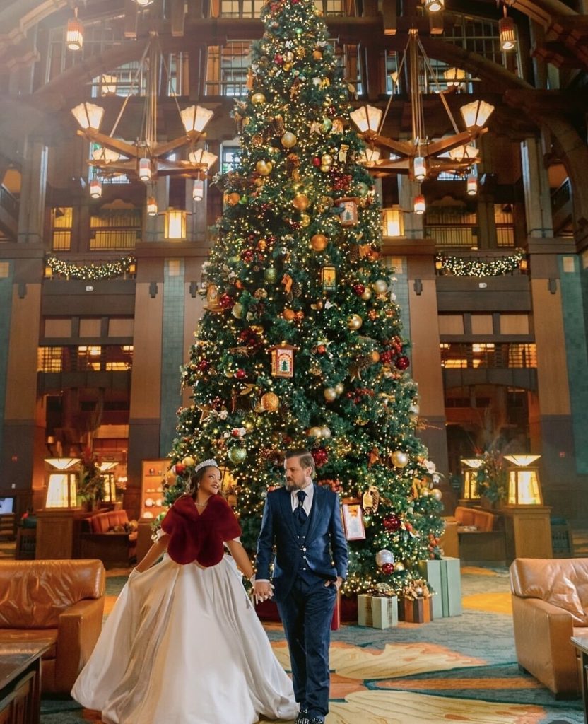 A couple holds hands in front of a Christmas tree at their winter wedding